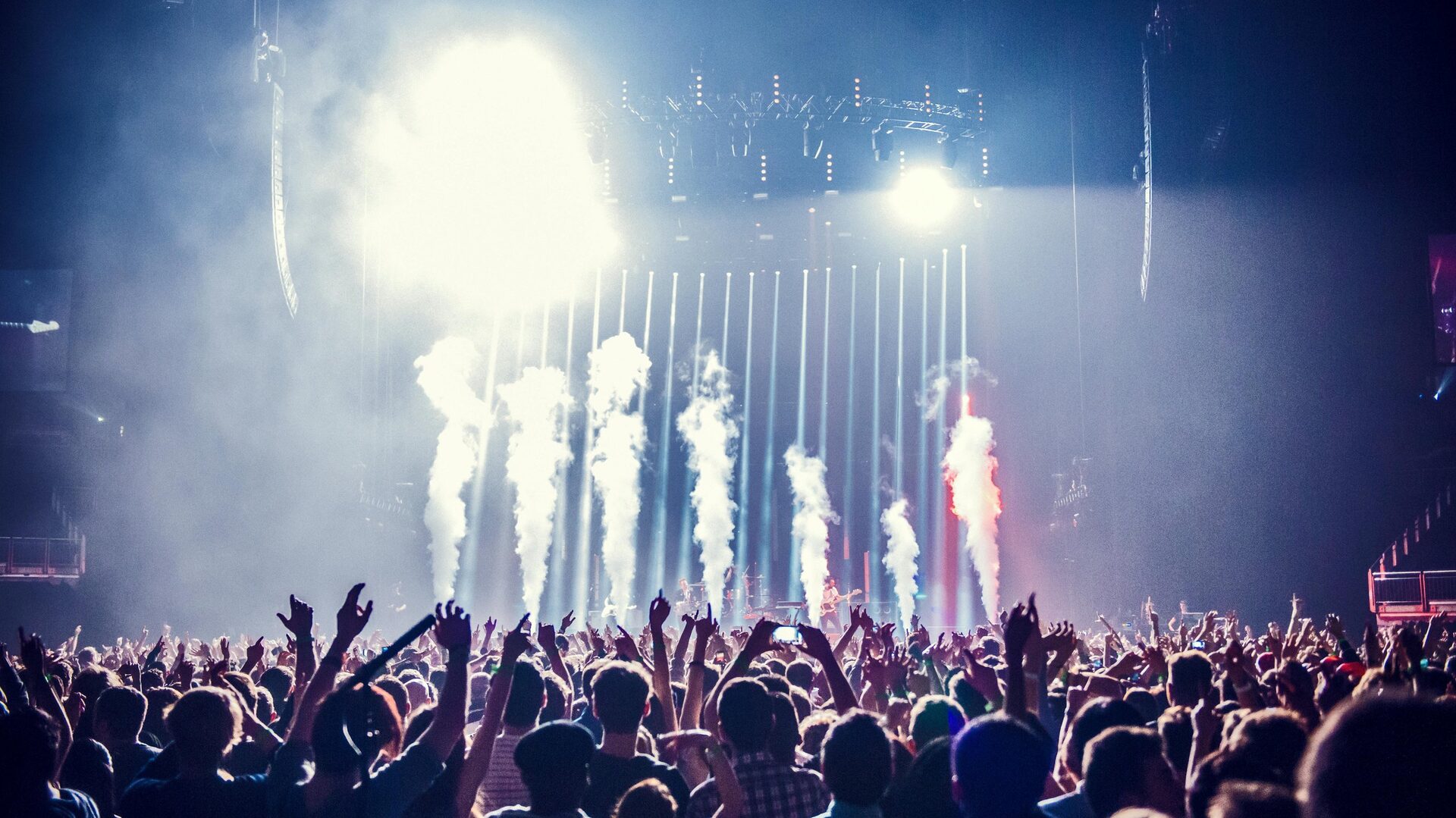 Massive concert stage with golden lighting beams cutting through atmospheric haze, crowd silhouettes at dusk
